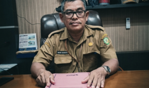 Pejabat Sekwan DPRD Kotawaringin Timur duduk di depan meja kerja dengan map berisi rincian dana perjalanan dinas.