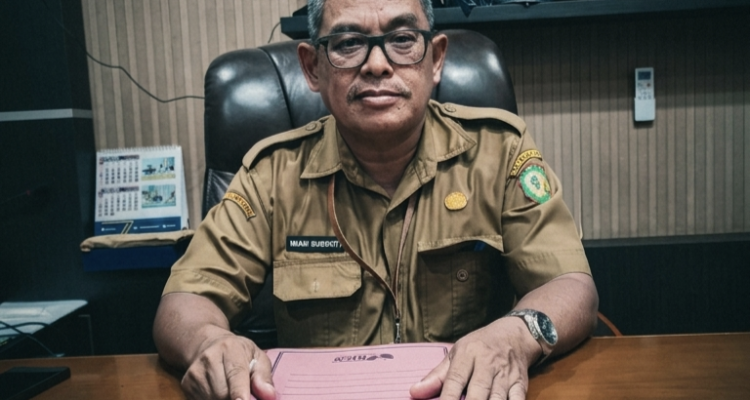 Pejabat Sekwan DPRD Kotawaringin Timur duduk di depan meja kerja dengan map berisi rincian dana perjalanan dinas.